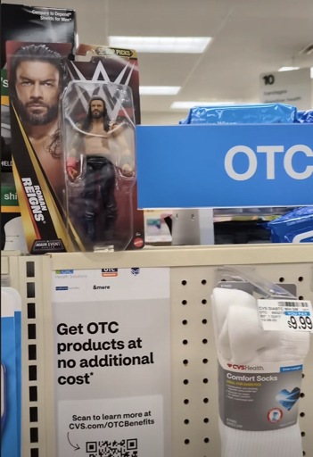 A shelf at CVS with various “OTC” ads with a Roman Reigns HWWE wrestler) on top of the shelf space, apparently added as a visual gag.